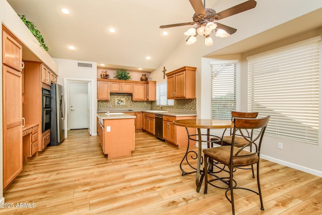 kitchen with light countertops, light wood-style flooring, decorative backsplash, appliances with stainless steel finishes, and a kitchen island