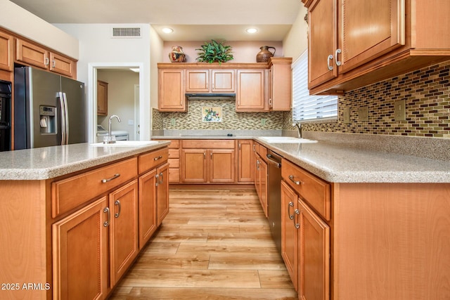 kitchen featuring stainless steel appliances, light wood finished floors, a sink, and light countertops