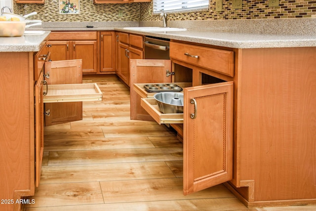 kitchen with tasteful backsplash, light countertops, light wood-style floors, brown cabinetry, and a sink