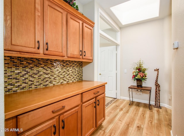 kitchen featuring brown cabinets, light wood finished floors, light countertops, decorative backsplash, and baseboards