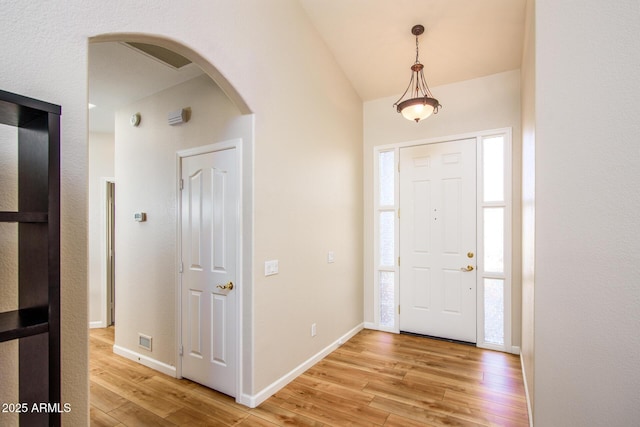 entryway featuring visible vents, arched walkways, baseboards, lofted ceiling, and light wood-style flooring