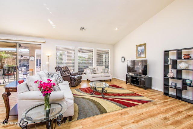 living area with high vaulted ceiling, wood finished floors, visible vents, and baseboards