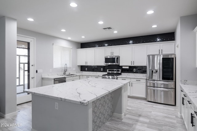 kitchen featuring stainless steel appliances, light stone countertops, sink, white cabinets, and a center island