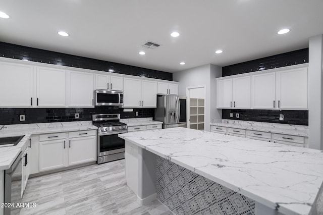 kitchen with white cabinets, light stone counters, appliances with stainless steel finishes, and backsplash