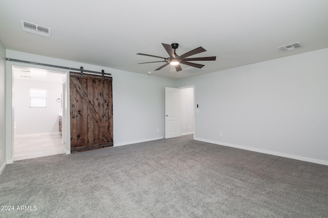 empty room featuring a barn door, ceiling fan, and carpet flooring