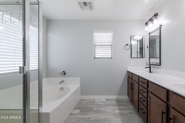 bathroom featuring a wealth of natural light, vanity, and tiled bath