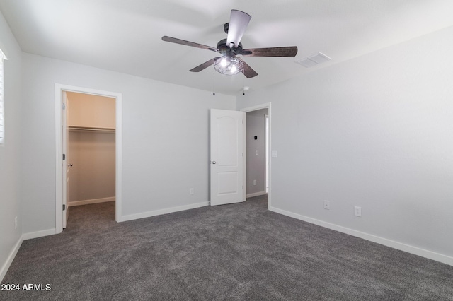 unfurnished bedroom featuring a closet, a walk in closet, dark carpet, and ceiling fan