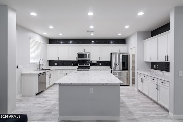 kitchen featuring stainless steel appliances, a center island, sink, light stone countertops, and white cabinetry