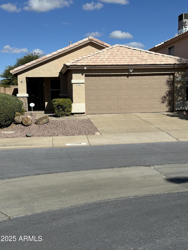 view of front of house with central air condition unit, a garage, driveway, a tiled roof, and stucco siding