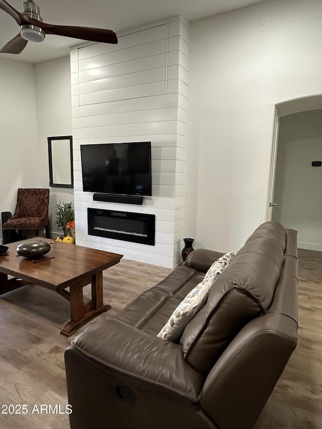 living area with a large fireplace, ceiling fan, and wood finished floors