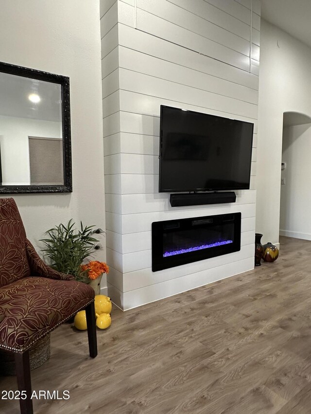 living room with arched walkways, a glass covered fireplace, and wood finished floors