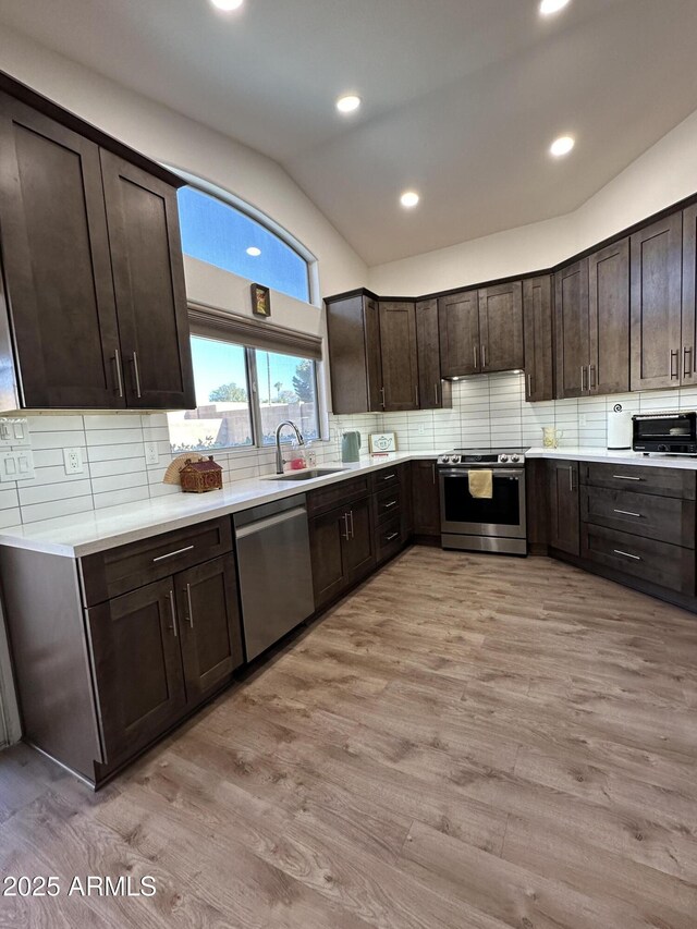 kitchen featuring decorative backsplash, appliances with stainless steel finishes, a sink, dark brown cabinets, and light wood-type flooring