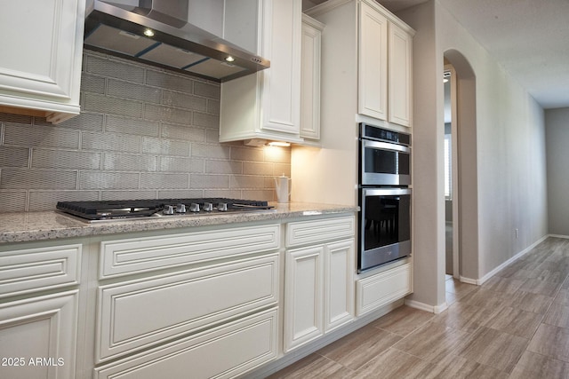 26421 W Zachary Dr, Buckeye, AZ 85396 - kitchen with tasteful backsplash, white cabinets, arched walkways, wall chimney exhaust hood, and stainless steel appliances