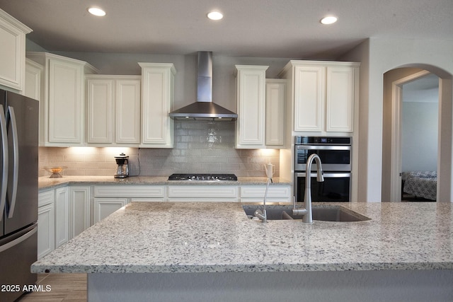 26421 W Zachary Dr, Buckeye, AZ 85396 - kitchen featuring wall chimney range hood, arched walkways, light stone counters, and stainless steel appliances