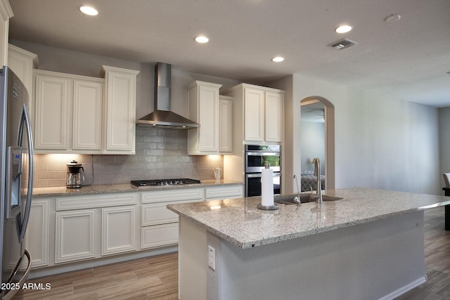 26421 W Zachary Dr, Buckeye, AZ 85396 - kitchen with arched walkways, light wood-type flooring, wall chimney range hood, appliances with stainless steel finishes, and a sink