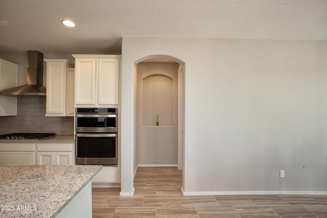 26421 W Zachary Dr, Buckeye, AZ 85396 - kitchen with tasteful backsplash, wall chimney exhaust hood, gas stovetop, arched walkways, and double oven