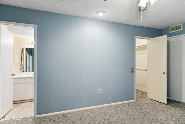 unfurnished bedroom featuring light carpet, ceiling fan, connected bathroom, and a textured ceiling