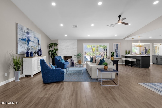 living room featuring a fireplace, ceiling fan with notable chandelier, hardwood / wood-style flooring, and vaulted ceiling