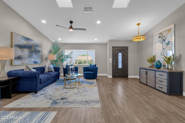 living room featuring hardwood / wood-style floors, ceiling fan with notable chandelier, and vaulted ceiling with skylight