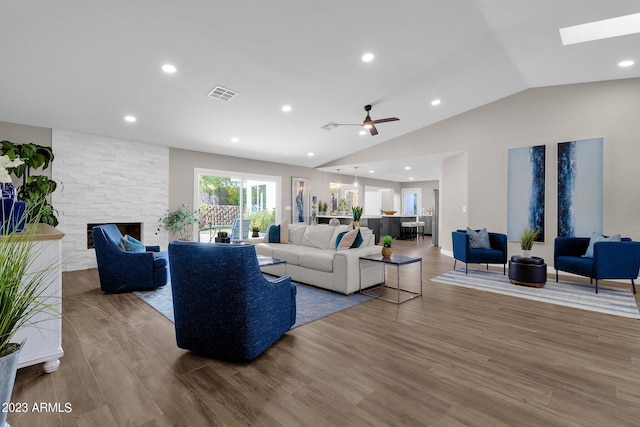 living room with a stone fireplace, ceiling fan, vaulted ceiling, and light hardwood / wood-style floors