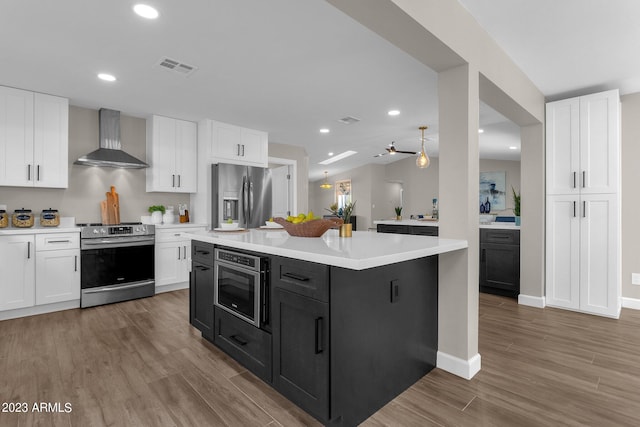 kitchen featuring white cabinets, wall chimney exhaust hood, light hardwood / wood-style flooring, a kitchen island, and appliances with stainless steel finishes