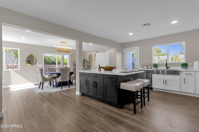 kitchen featuring white cabinets, hanging light fixtures, sink, and light hardwood / wood-style flooring