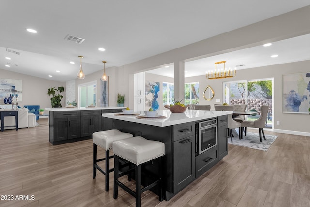 kitchen featuring a breakfast bar, decorative light fixtures, light hardwood / wood-style flooring, stainless steel microwave, and a kitchen island