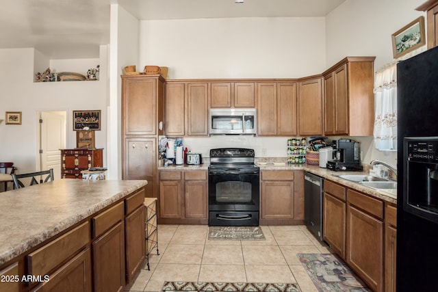 kitchen with a sink, light tile patterned floors, black appliances, and brown cabinets