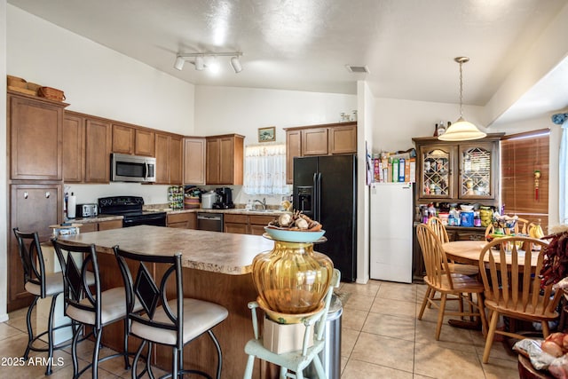 kitchen featuring brown cabinets, a sink, light tile patterned floors, a kitchen bar, and black appliances
