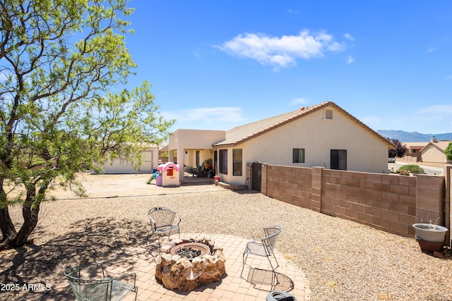 rear view of house featuring fence, stucco siding, a mountain view, a patio area, and a fire pit