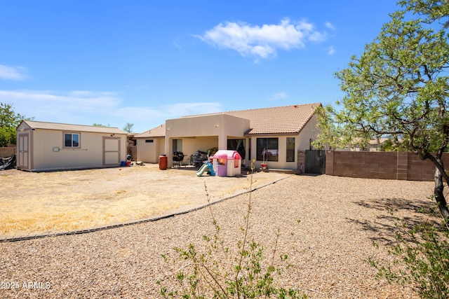 back of property featuring stucco siding, a shed, a fenced backyard, an outbuilding, and a tiled roof