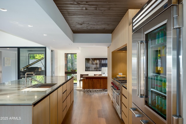 kitchen featuring high quality appliances, modern cabinets, wood finished floors, a sink, and stone countertops