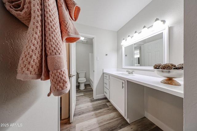 bathroom with toilet, vanity, wood finished floors, and baseboards