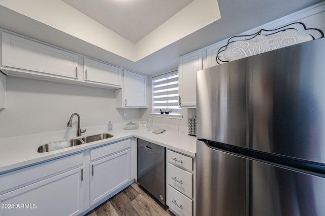 kitchen with light countertops, freestanding refrigerator, white cabinetry, dishwasher, and a sink