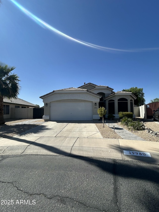 view of front facade featuring a garage, fence, concrete driveway, and stucco siding