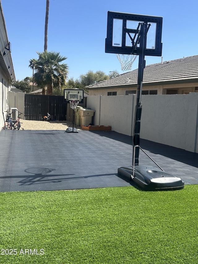 view of basketball court with a yard and a fenced backyard