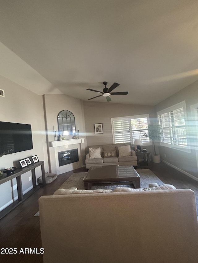 living room featuring visible vents, dark wood finished floors, lofted ceiling, a glass covered fireplace, and a ceiling fan