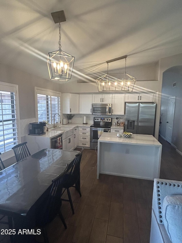 kitchen with a sink, tasteful backsplash, arched walkways, appliances with stainless steel finishes, and white cabinets