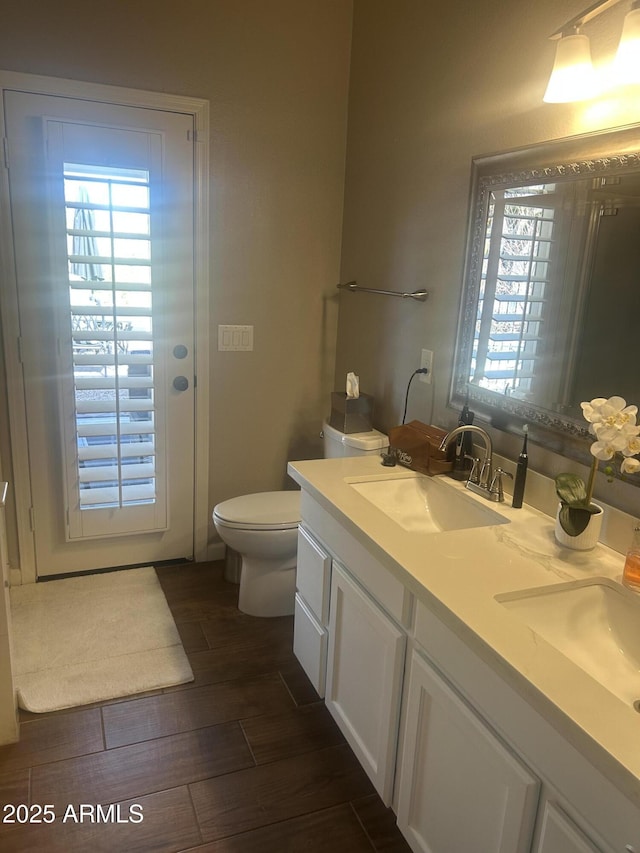 bathroom with a sink, toilet, wood finished floors, and double vanity