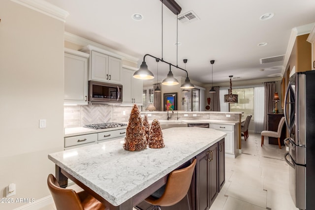 kitchen with a kitchen bar, decorative backsplash, stainless steel appliances, a kitchen island, and hanging light fixtures