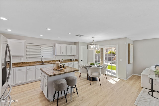 kitchen with a kitchen island, sink, white cabinets, hanging light fixtures, and stainless steel refrigerator with ice dispenser