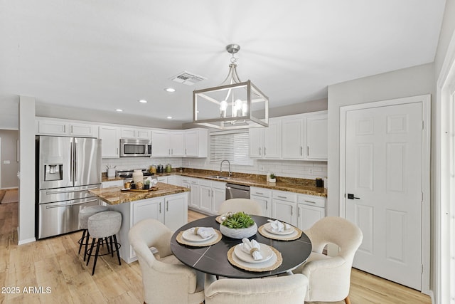 kitchen with sink, white cabinetry, hanging light fixtures, stainless steel appliances, and a kitchen island