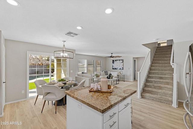 kitchen featuring stainless steel refrigerator, hanging light fixtures, light stone counters, light hardwood / wood-style floors, and white cabinets