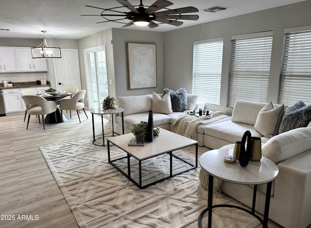 living room featuring ceiling fan with notable chandelier and light wood-type flooring