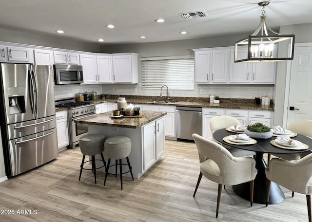 kitchen featuring a kitchen island, pendant lighting, white cabinetry, sink, and stainless steel appliances