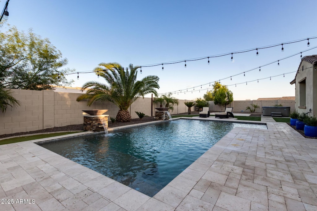 pool at dusk with a jacuzzi, pool water feature, and a patio