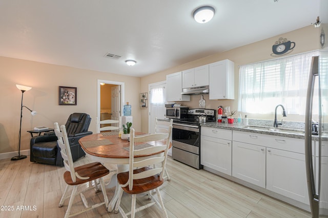 kitchen with white cabinets, appliances with stainless steel finishes, light hardwood / wood-style flooring, and light stone countertops