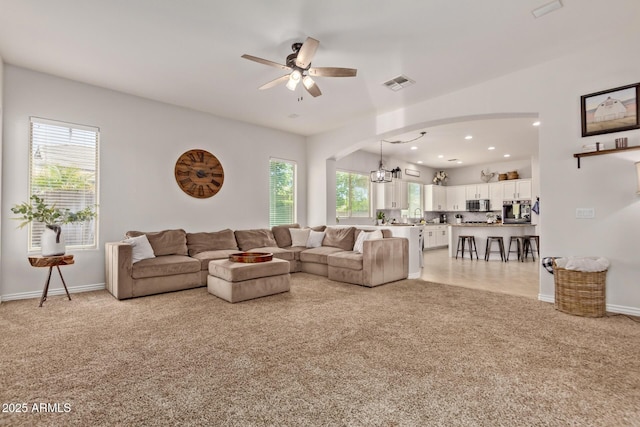 living room featuring light carpet, ceiling fan, arched walkways, a chandelier, and baseboards