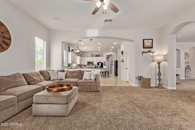 living room with a ceiling fan, light colored carpet, recessed lighting, arched walkways, and a chandelier