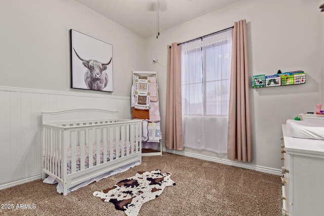 carpeted bedroom featuring a nursery area and wainscoting